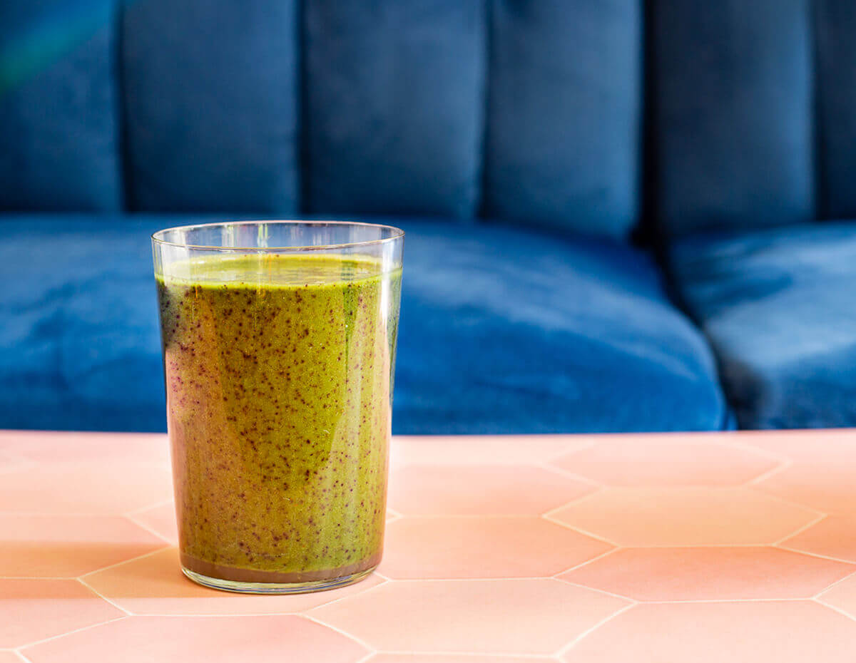 Spinach and Oat smoothie on a terra cotta tabletop with a blue velvet background